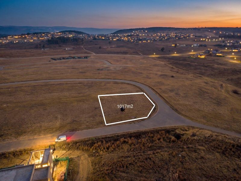 Aerial view of a 1017m2 vacant residential plot situated in a developing estate with paved road access and scenic landscape views.