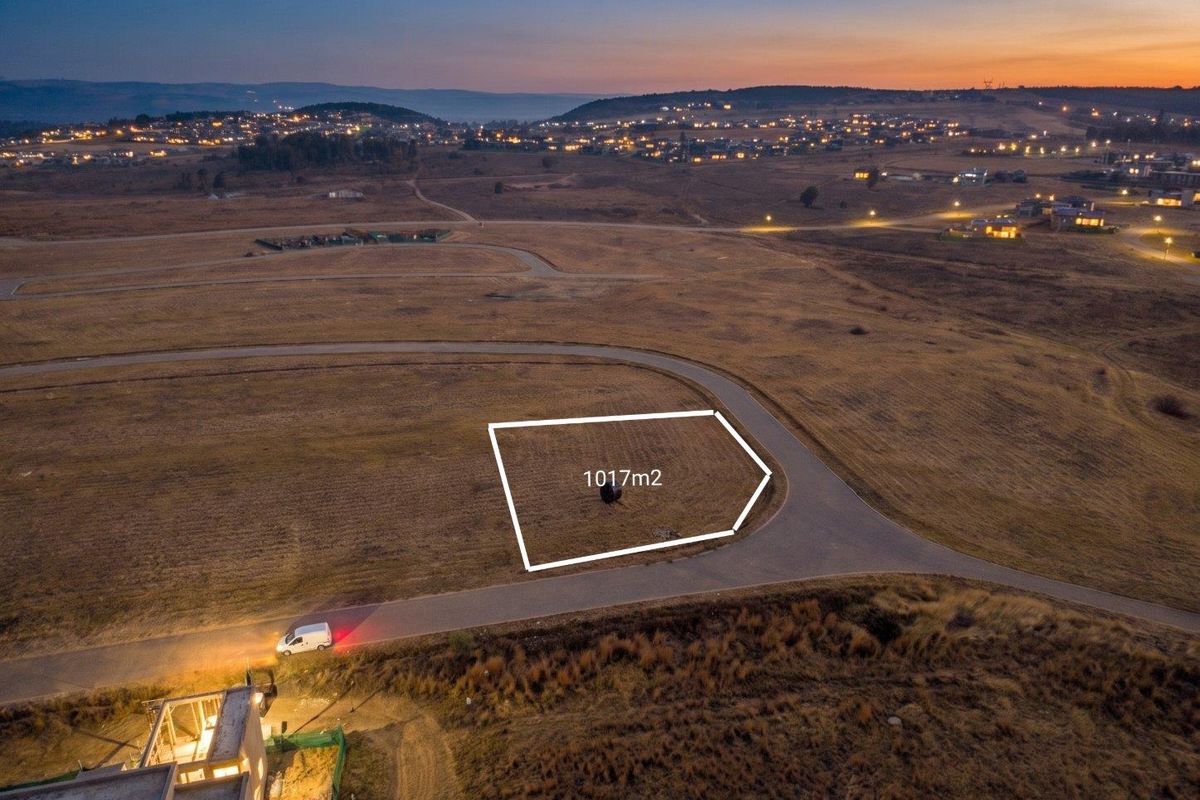 Aerial view of a 1017m2 vacant residential plot situated in a developing estate with paved road access and scenic landscape views.