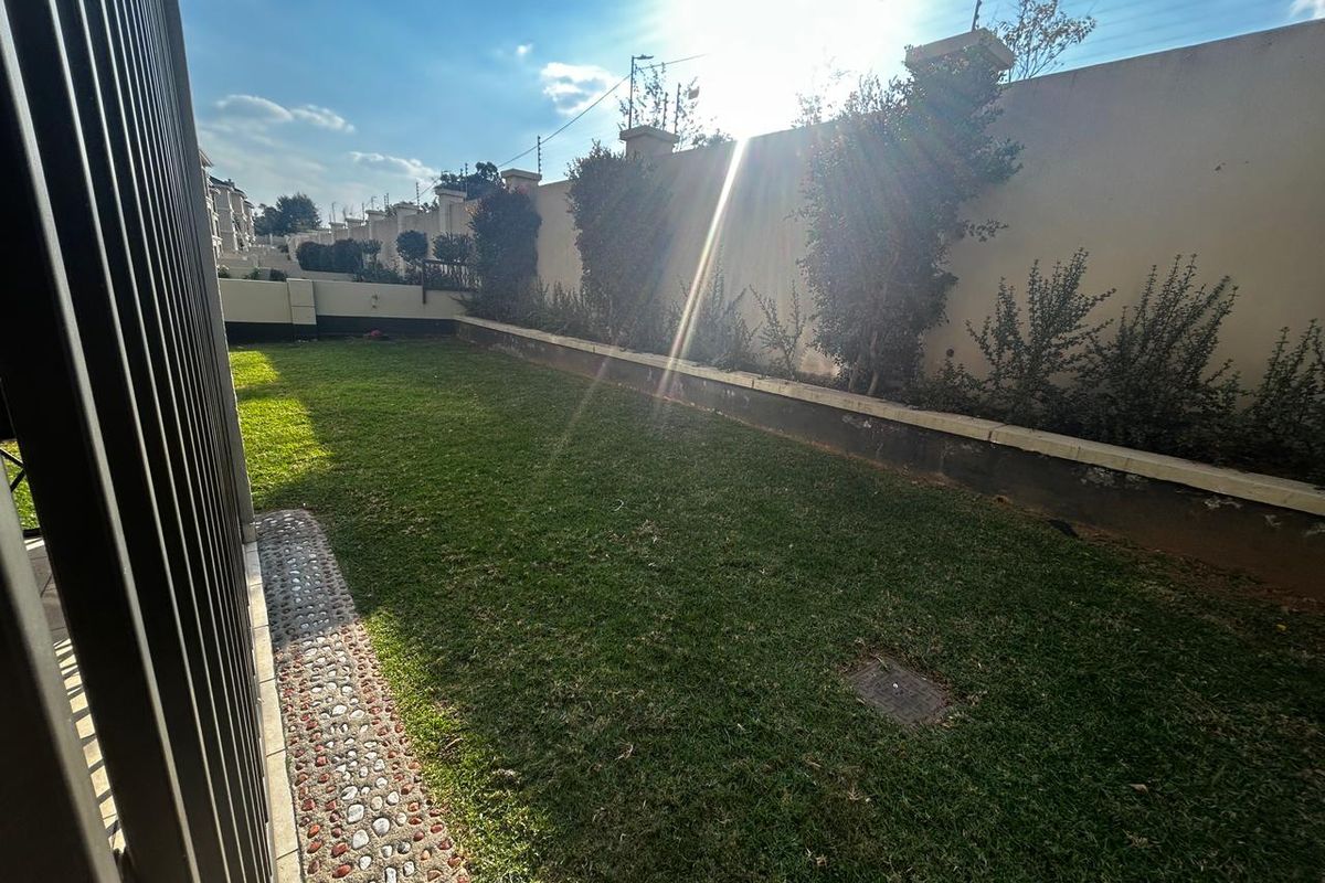A private rear garden area featuring a lawn, perimeter boundary wall, and stone-lined pathway.