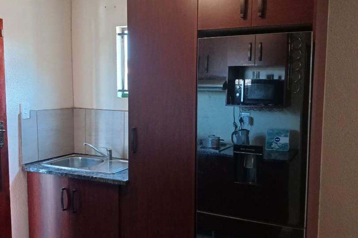 A compact kitchen area featuring dark wood-finish cabinetry, a stainless steel sink, and tiled flooring.