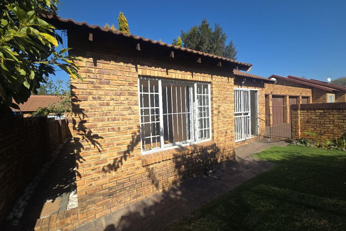 Rear view of the townhouse featuring face-brick exterior, tiled roof, security bars on windows, and a small private garden area.