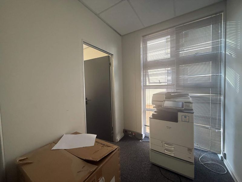A functional office space featuring a suspended ceiling, carpeted flooring, and large windows with venetian blinds, providing a clean and professional work environment.