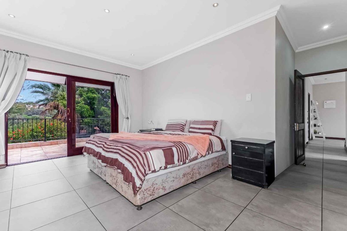 Spacious bedroom featuring large format floor tiles, recessed downlighting, and sliding glass doors opening onto a private balcony with scenic views.