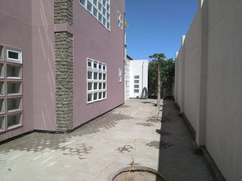 A side courtyard area featuring paved flooring, stone-clad exterior walls, and multi-pane windows, enclosed by a high boundary wall.