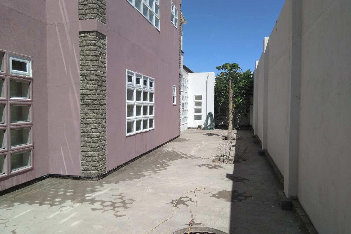 A side courtyard area featuring paved flooring, stone-clad exterior walls, and multi-pane windows, enclosed by a high boundary wall.