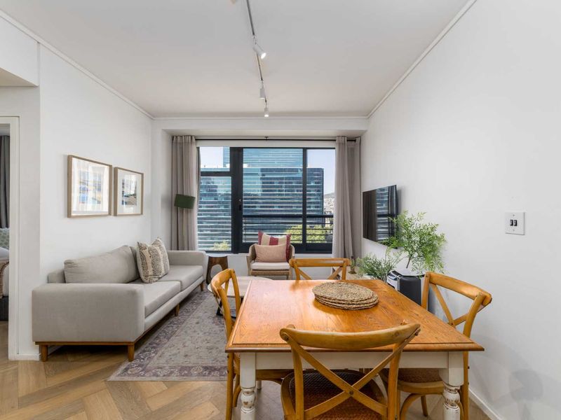 Bright open-plan living and dining area featuring elegant herringbone timber flooring, modern track lighting, and large windows with urban views.