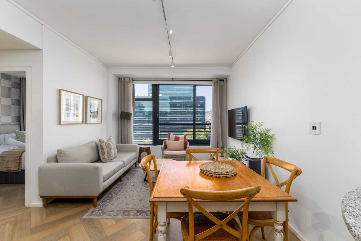 Bright open-plan living and dining area featuring elegant herringbone timber flooring, modern track lighting, and large windows with urban views.