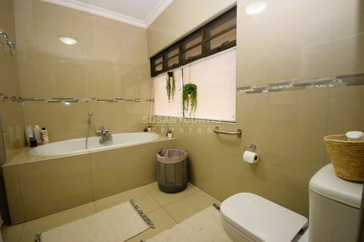 A functional bathroom featuring a built-in bathtub with shower mixer, tiled walls, and a window with fitted blinds.