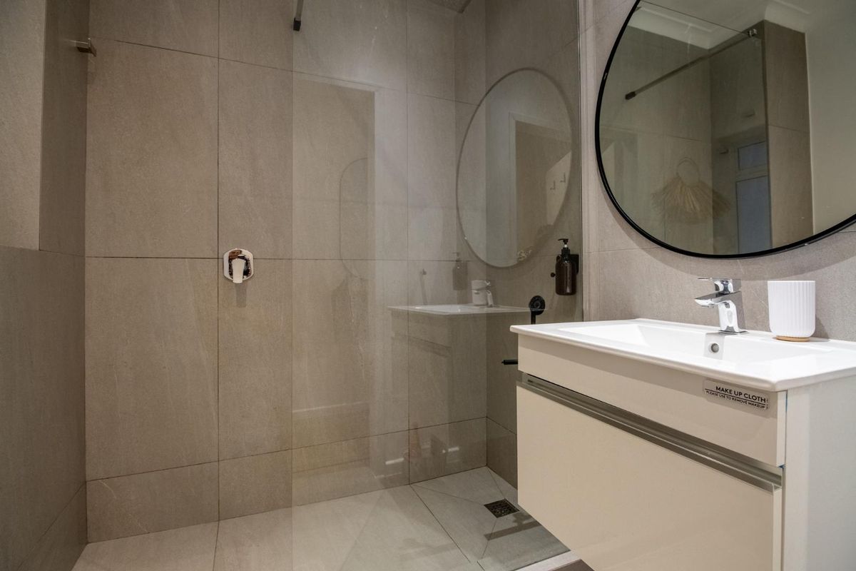 Modern bathroom featuring a walk-in shower with glass screen, wall-mounted vanity with basin, and contemporary large-format tiling.