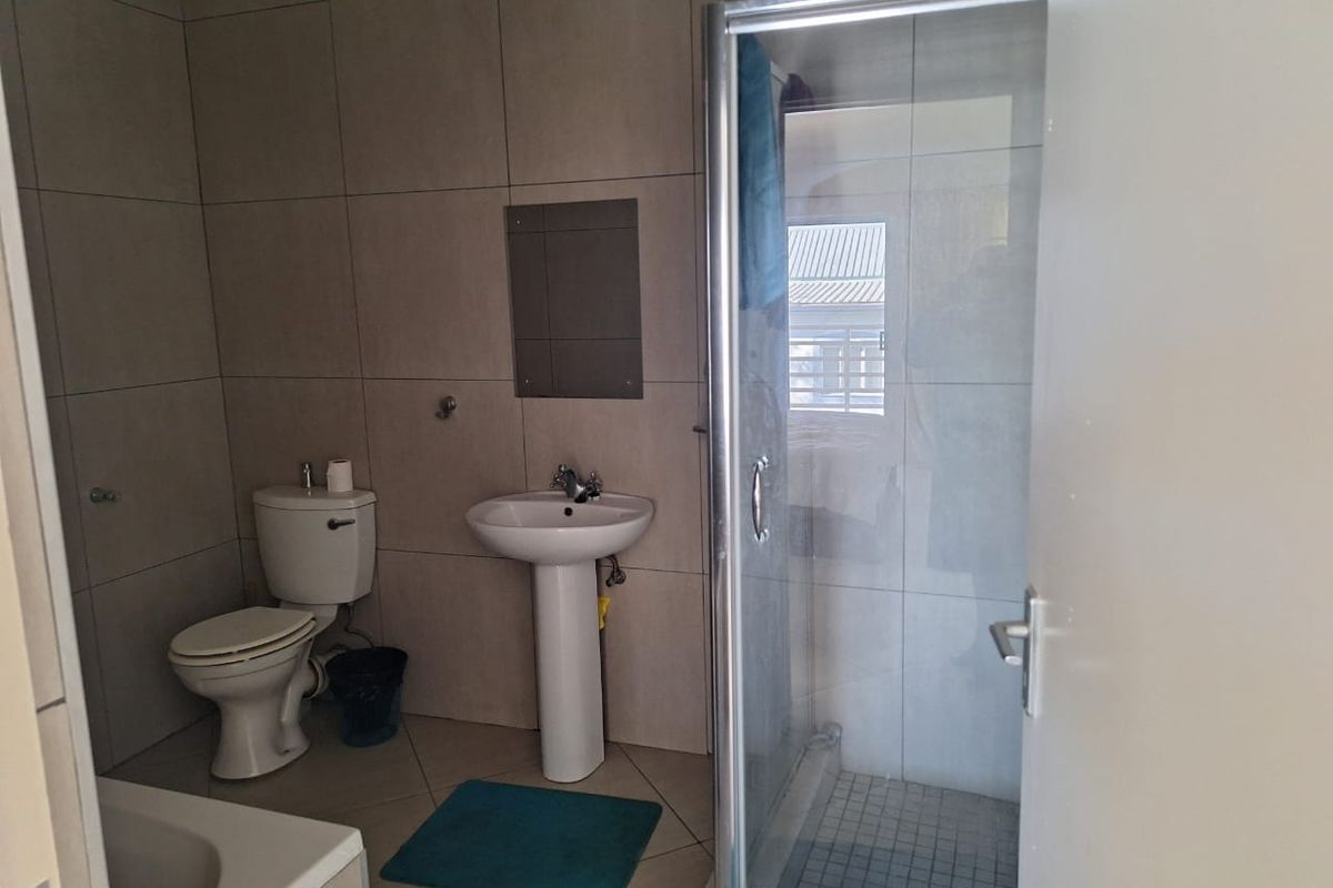 A functional bathroom featuring a pedestal washbasin, toilet, shower enclosure with glass door, and a bathtub, finished with neutral wall and floor tiles.
