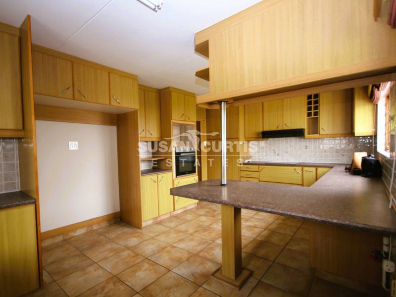 A functional kitchen featuring wood-finish cabinetry, tiled flooring, a breakfast bar, and built-in appliances including an oven and extractor fan.