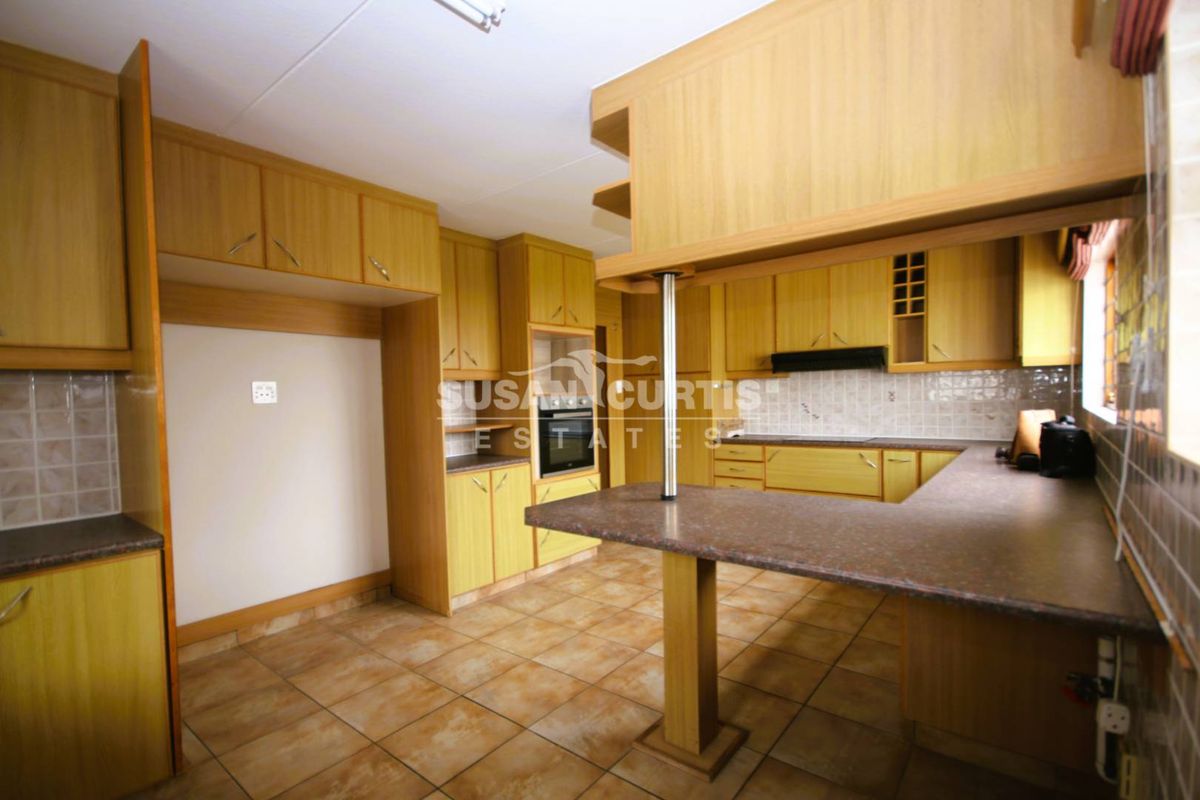 A functional kitchen featuring wood-finish cabinetry, tiled flooring, a breakfast bar, and built-in appliances including an oven and extractor fan.