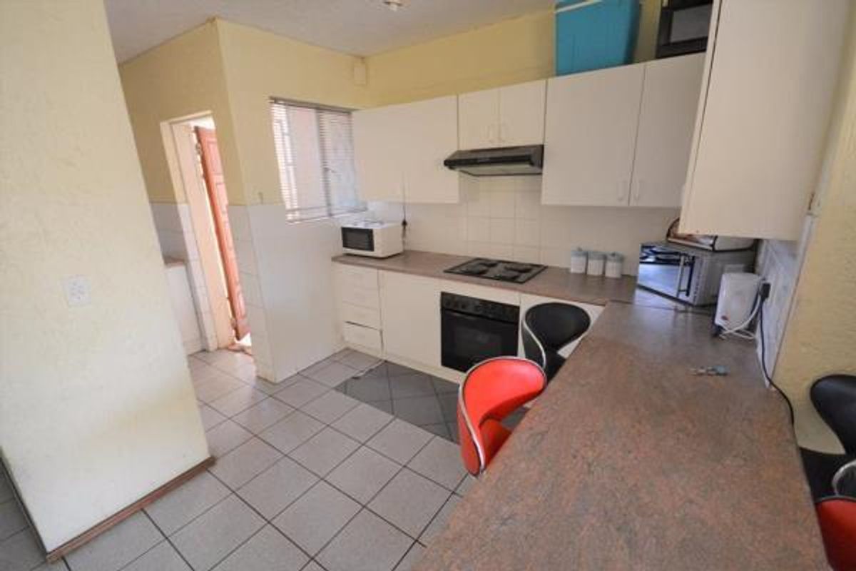A functional kitchen featuring white cabinetry, a built-in oven, hob, and extractor fan, with a breakfast bar and tiled flooring.