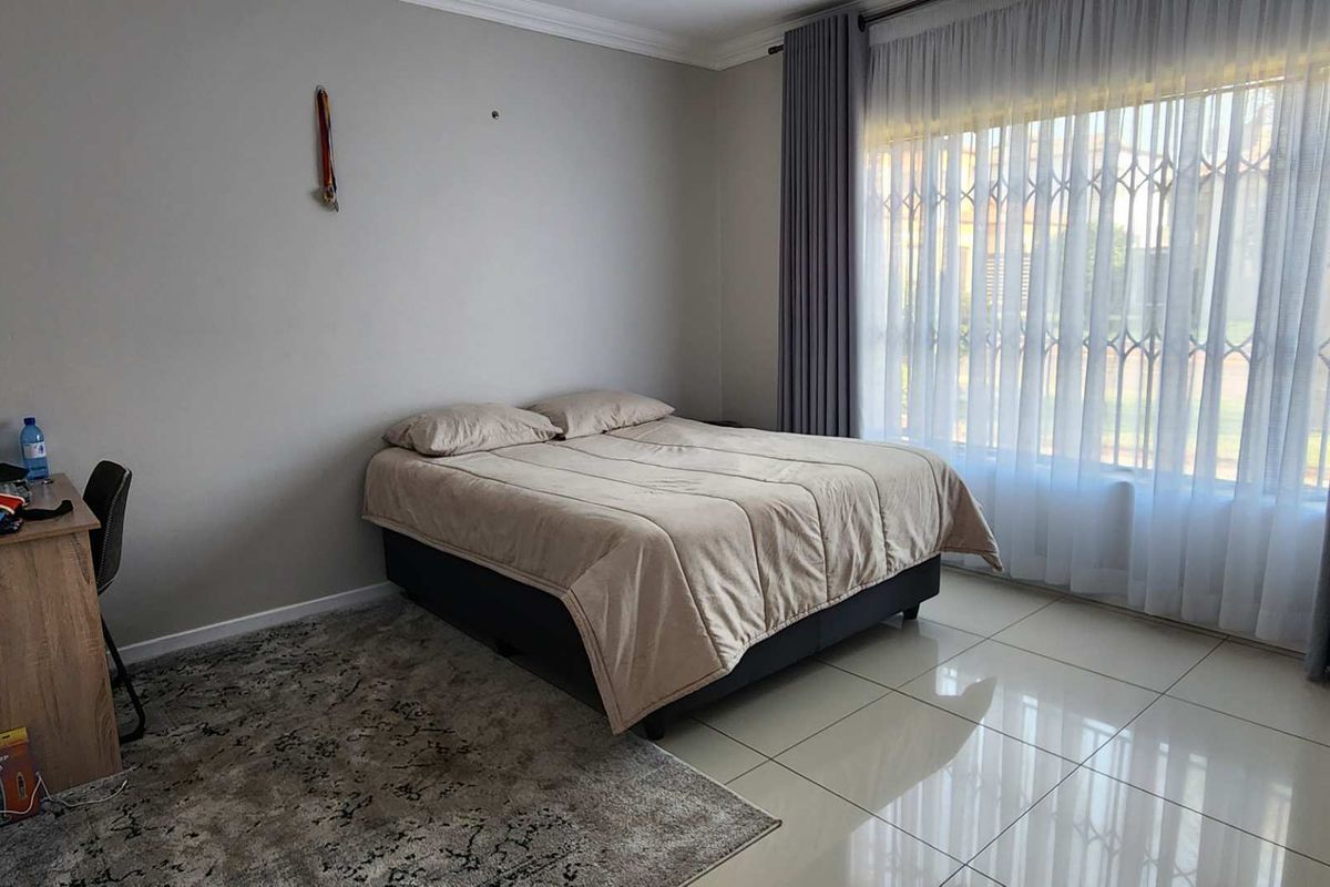A well-lit bedroom featuring large windows with security bars, neutral tiled flooring, and crown molding.