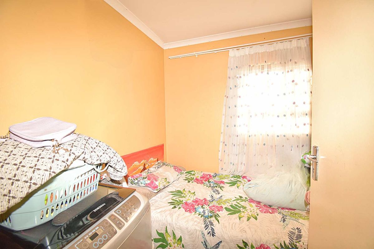 A compact bedroom featuring a window with curtain track and standard door, currently utilized with a bed and laundry appliance.
