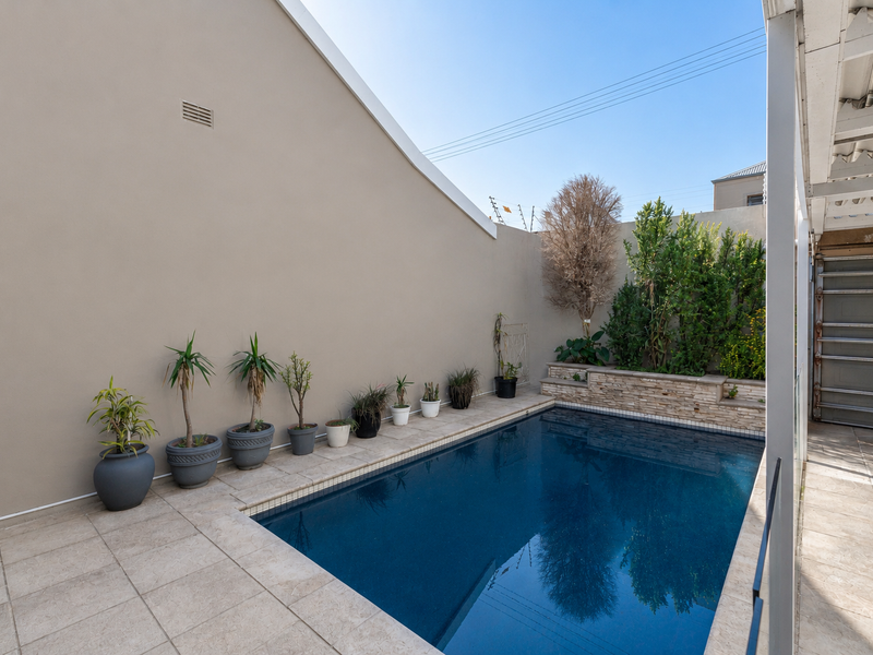 A well-maintained outdoor pool area featuring a tiled surround, stone-clad planter box, and a covered patio space.