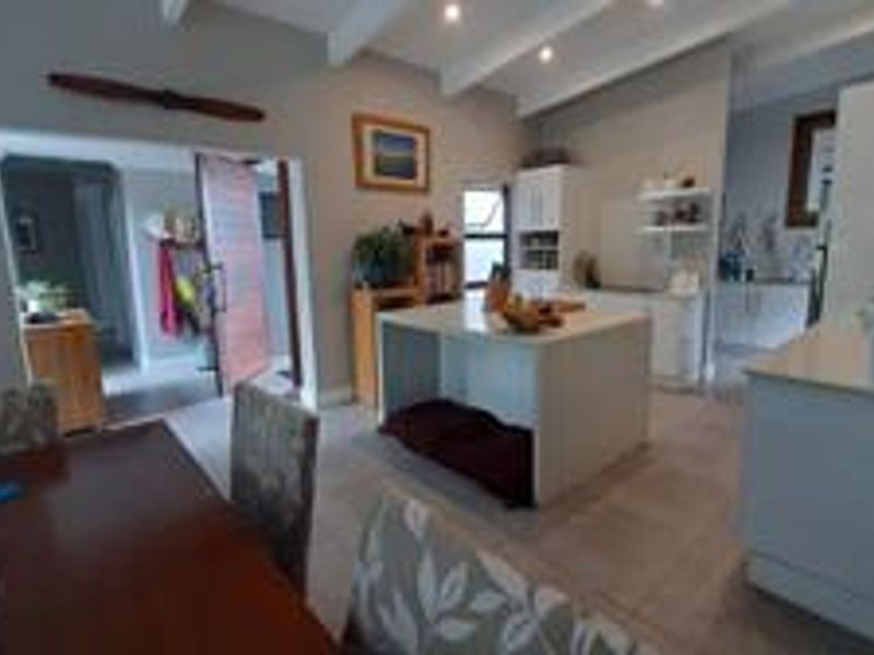 Open-plan living and kitchen area featuring a central island, exposed ceiling beams, and tiled flooring, creating a bright and functional space.