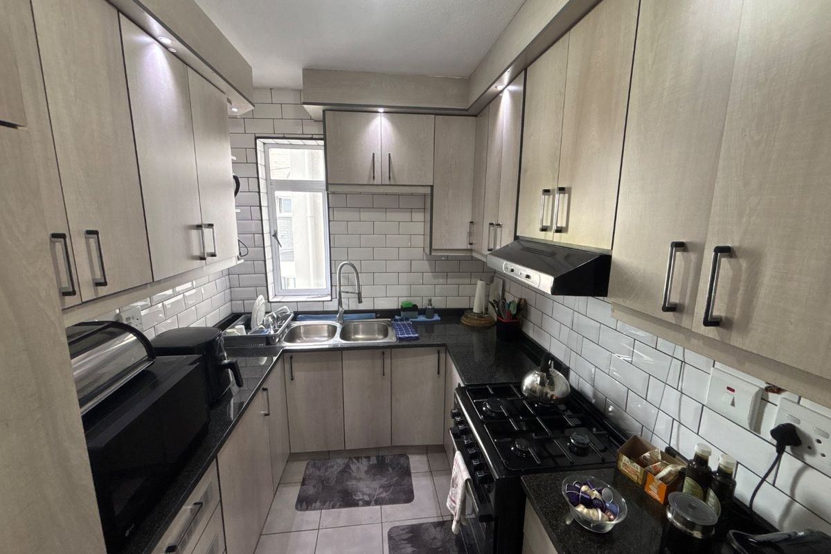 A well-maintained galley kitchen featuring light wood-finish cabinetry, black granite countertops, subway tile backsplash, and a gas stove with an integrated extractor fan.