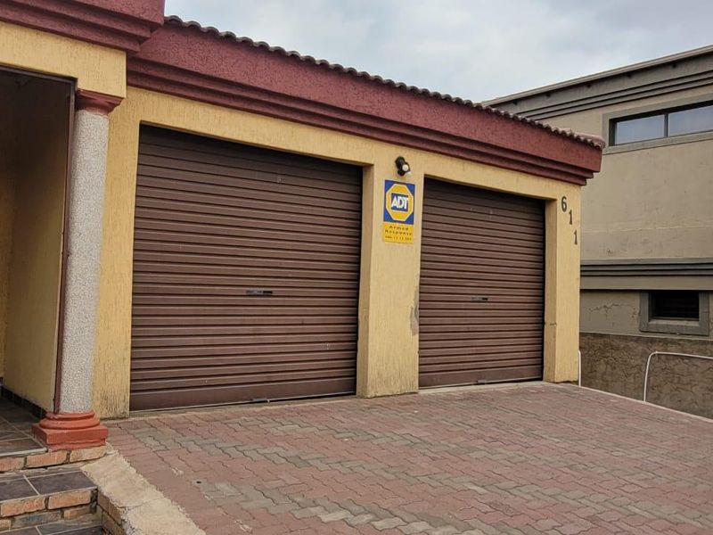 A double garage featuring brown roller doors and a paved driveway, situated at the front entrance of the property.