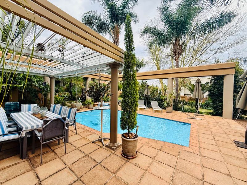 Outdoor pool area featuring a tiled patio, structural pergola, and established garden surroundings, ideal for relaxation and entertainment.