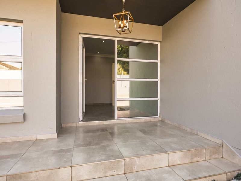 A modern, well-maintained entrance porch featuring large format floor tiles, a contemporary glass-panelled front door, and a stylish pendant light fixture.