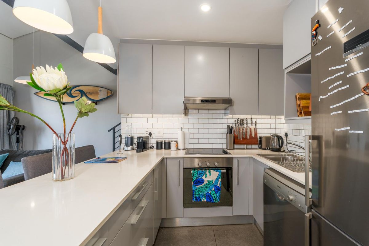 Modern kitchen featuring grey cabinetry, white subway tile backsplash, stone countertops, integrated oven, hob, and extractor fan, with an adjoining breakfast bar.