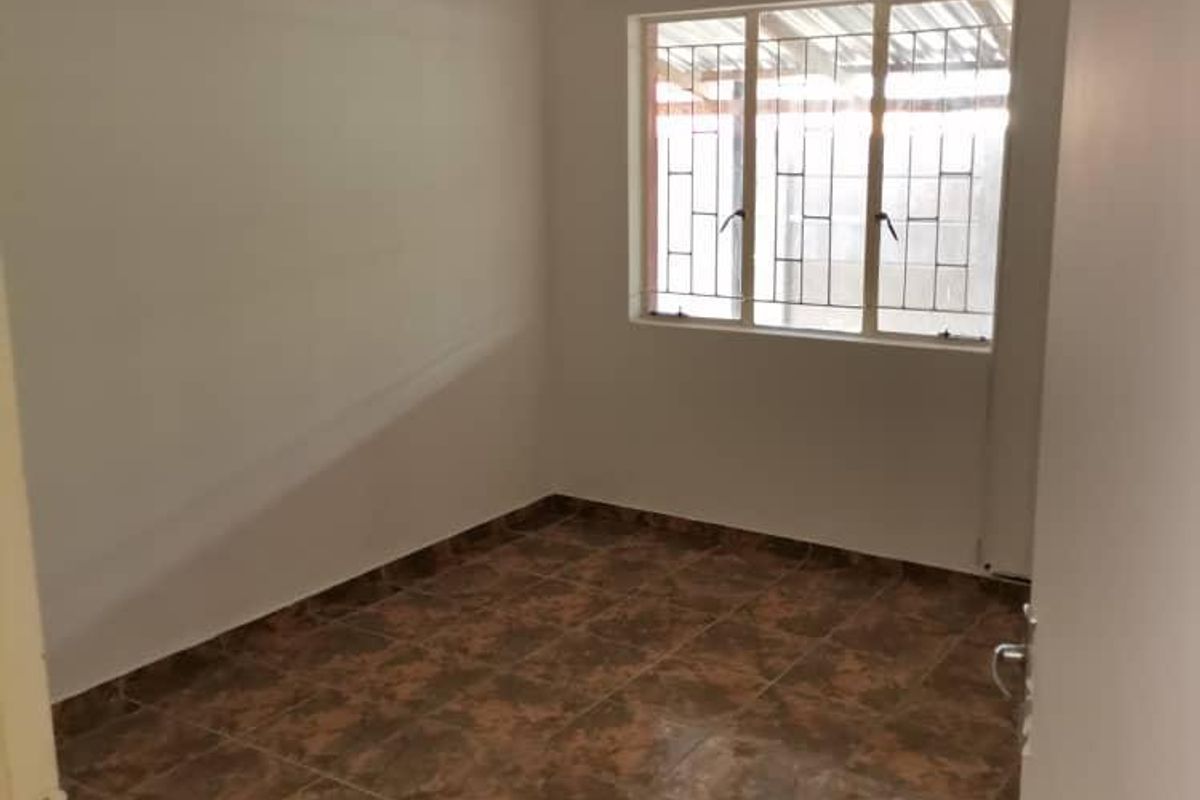 A clean, empty bedroom featuring tiled flooring and a window with security bars, offering a neutral space ready for personalization.