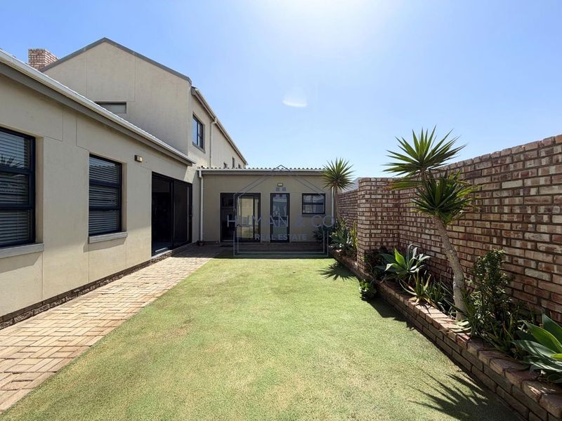 A well-maintained rear garden featuring a paved walkway, artificial lawn, and a brick boundary wall, providing a clean and low-maintenance outdoor space.