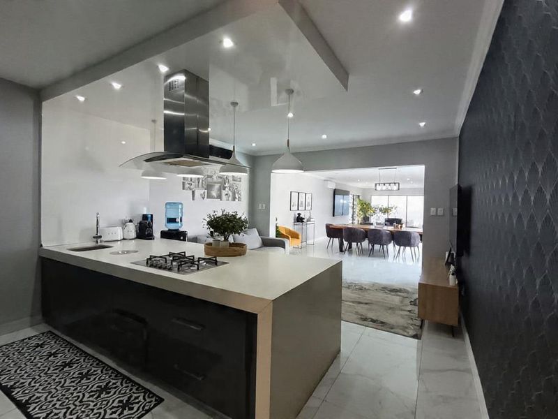 Modern open-plan living area featuring a sleek kitchen island with gas hob, integrated extractor, and seamless flow into the dining and lounge spaces.