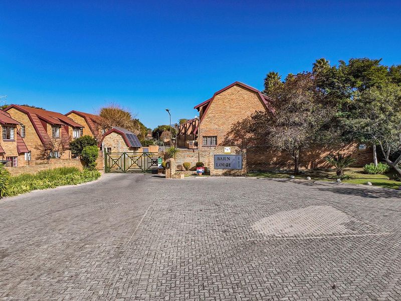 Front entrance view of Barn Lodge townhouse complex featuring a paved driveway, brick facade buildings, and secure gated access.