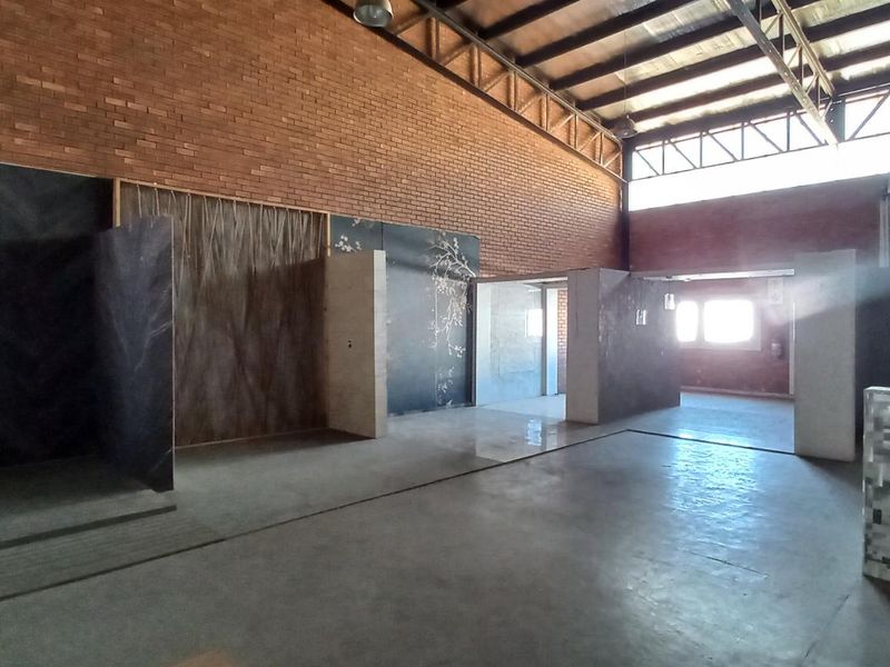 Spacious industrial warehouse interior featuring exposed brick walls, high steel truss ceilings, polished concrete flooring, and multiple partitioned display areas.