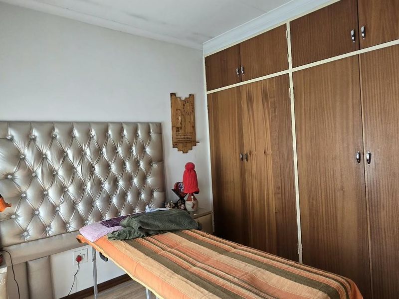 Bedroom featuring built-in wooden cupboards and laminate flooring, currently utilized as a treatment room. Note visible ceiling damage requiring repair.