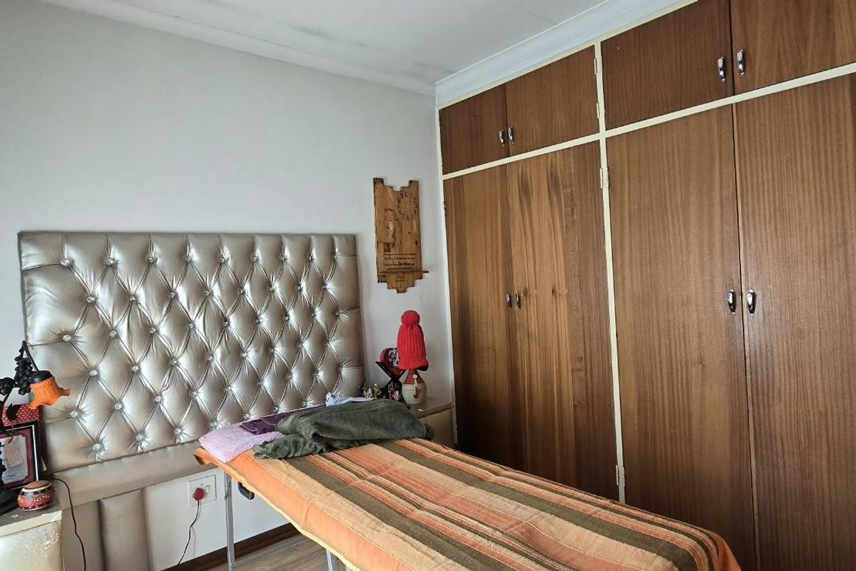 Bedroom featuring built-in wooden cupboards and laminate flooring, currently utilized as a treatment room. Note visible ceiling damage requiring repair.