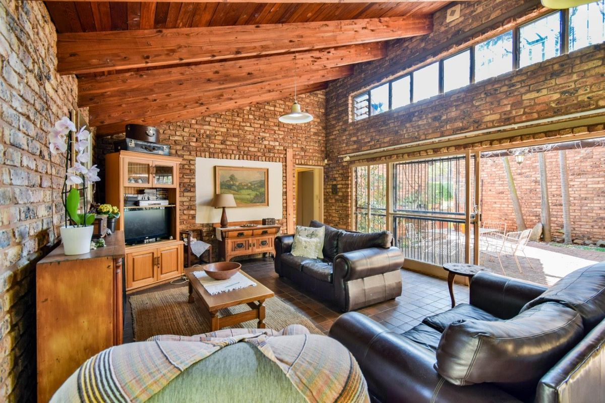 Spacious living room featuring exposed timber beam ceilings, rustic face-brick walls, and large sliding glass doors opening to an outdoor patio area.