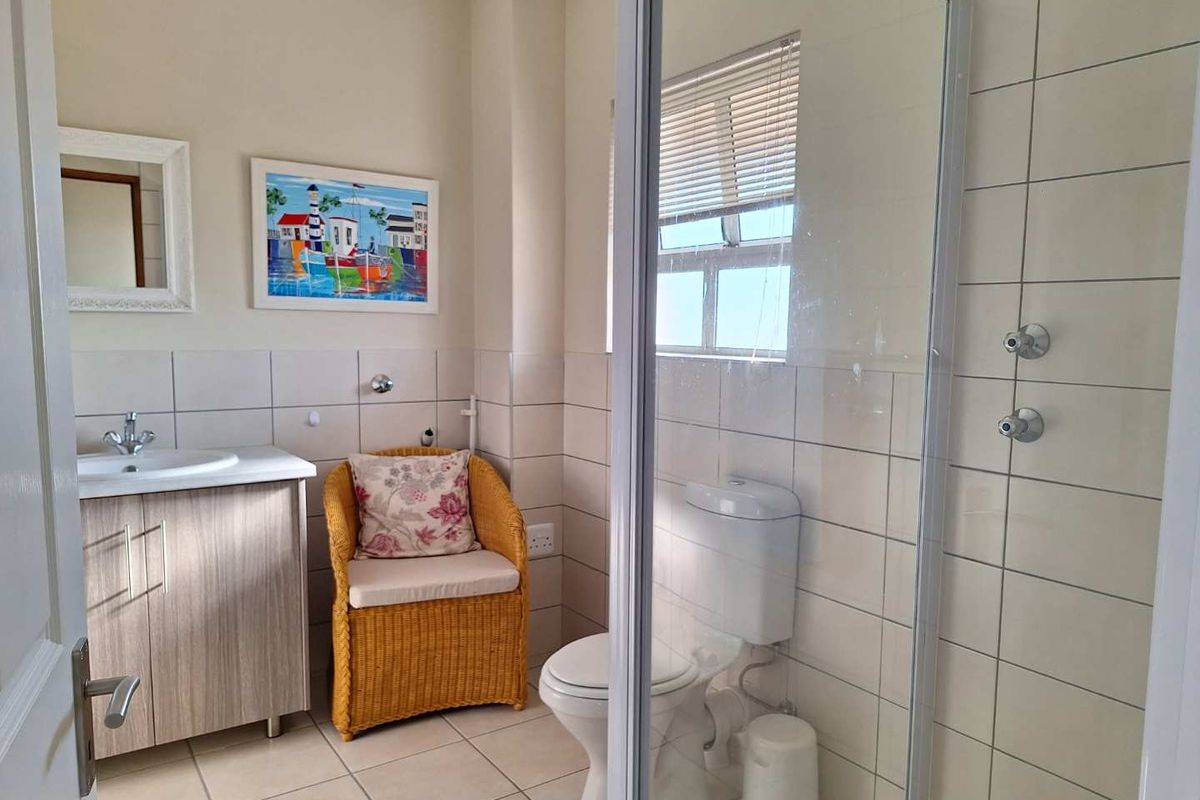 A functional bathroom featuring a glass-enclosed shower, a vanity with a basin, and a toilet, finished with neutral wall and floor tiles.
