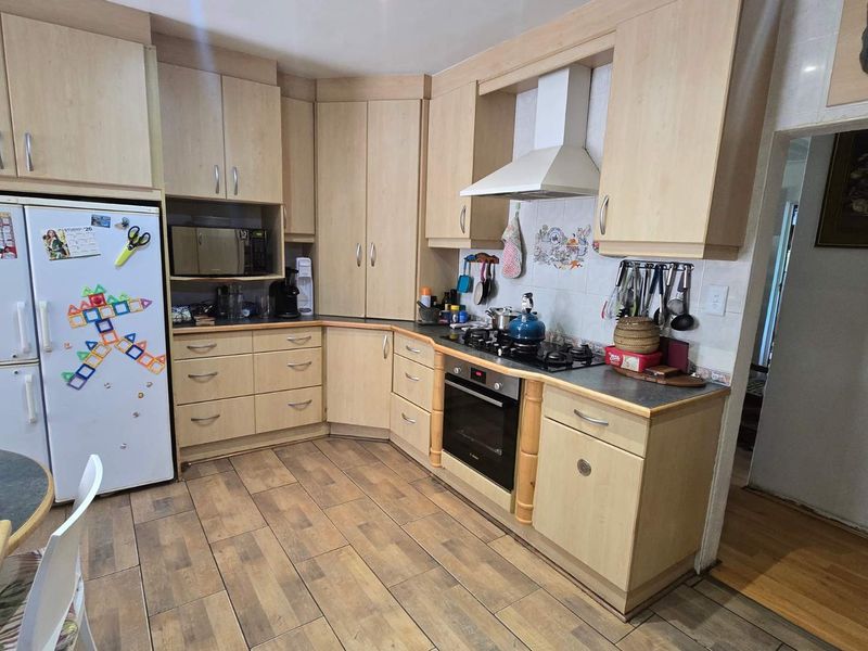 A functional kitchen featuring light wood-finish cabinetry, integrated appliances including an oven and gas hob, and durable tiled flooring.
