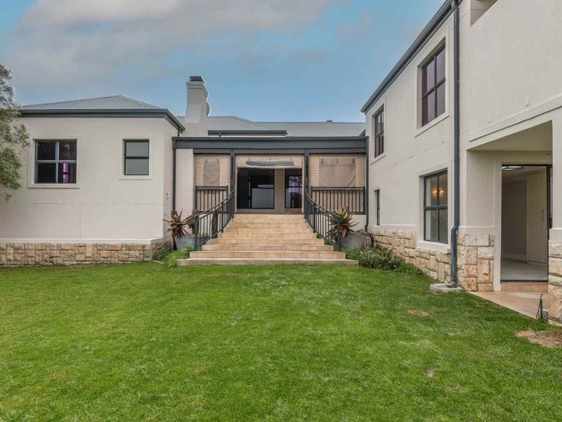 Rear view of a two-story house featuring stone cladding, a central staircase leading to a covered patio, and a well-maintained lawn.
