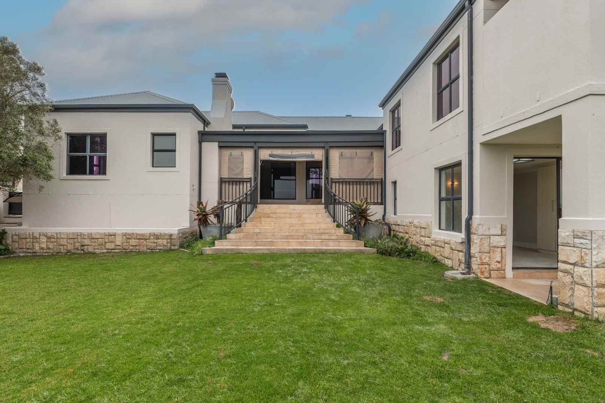 Rear view of a two-story house featuring stone cladding, a central staircase leading to a covered patio, and a well-maintained lawn.