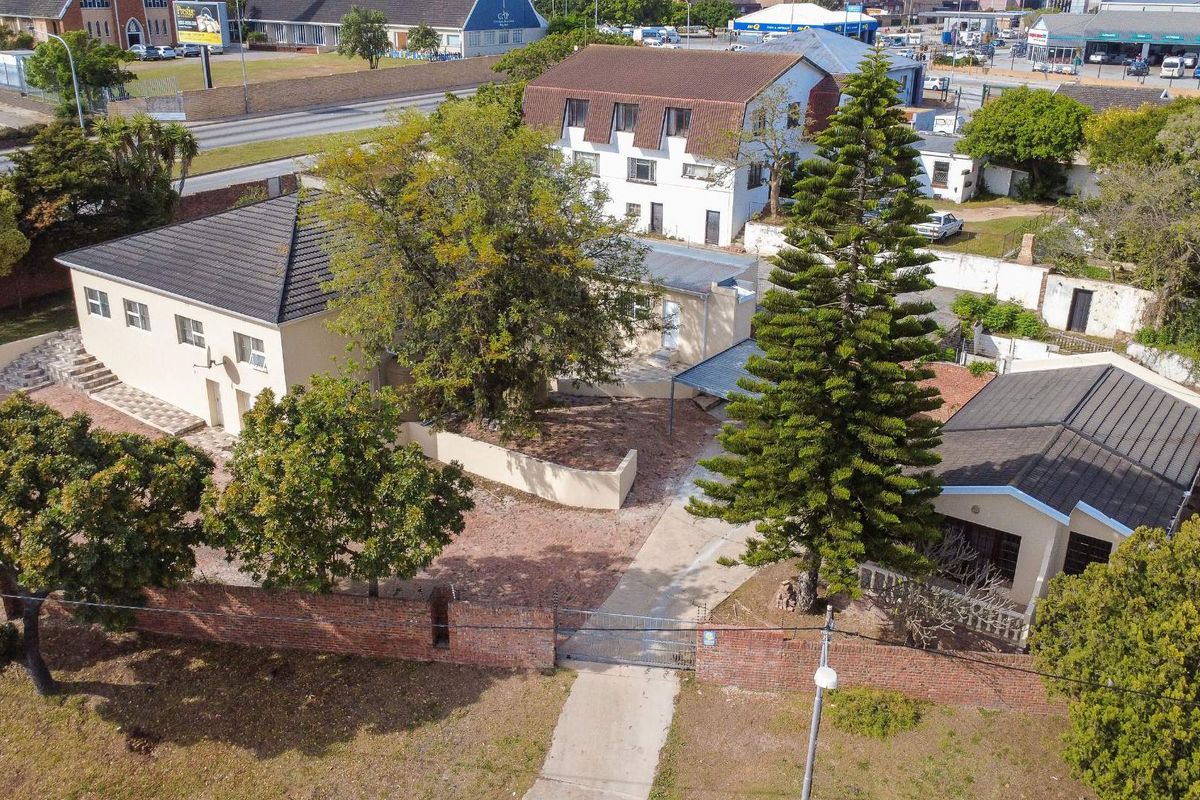 Aerial view of the property showing the main building, driveway, mature trees, and brick boundary wall with gated access.