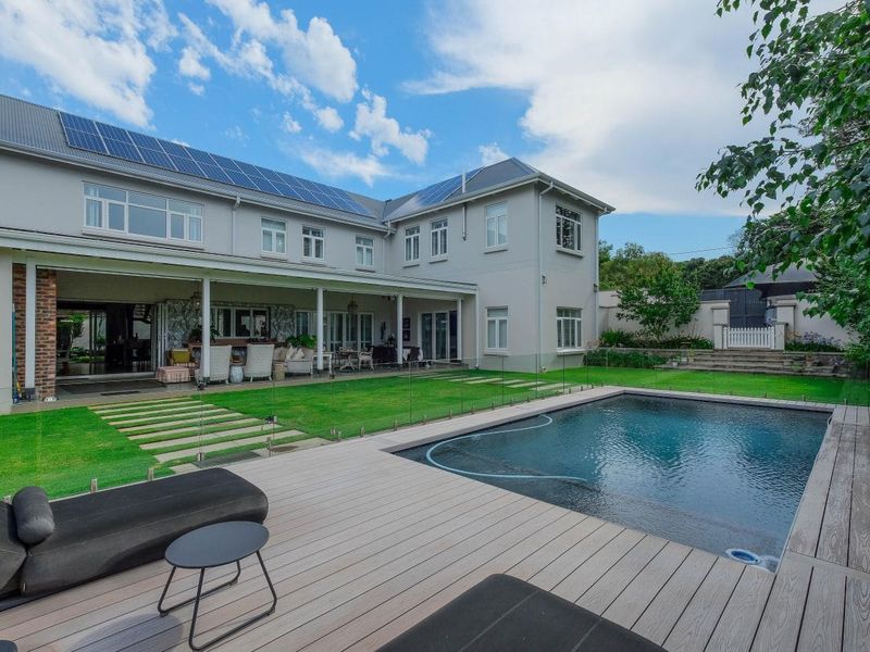 Spacious rear exterior featuring a swimming pool, timber decking, covered patio, and solar panels on the roof, set within a well-maintained garden.