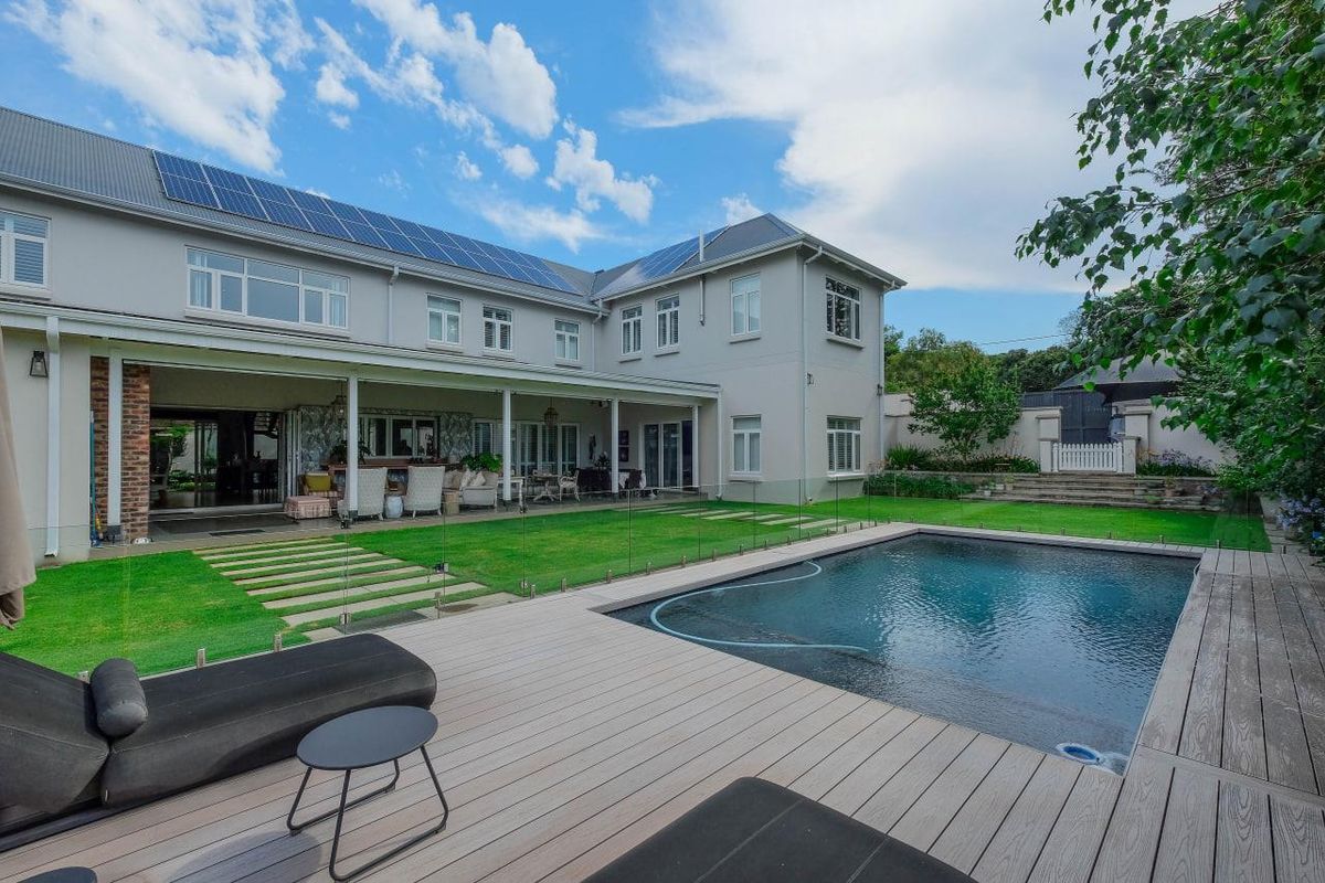 Spacious rear exterior featuring a swimming pool, timber decking, covered patio, and solar panels on the roof, set within a well-maintained garden.