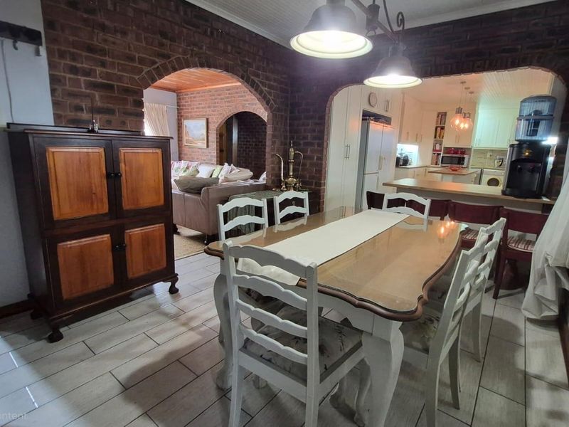Open-plan dining and kitchen area featuring exposed brick walls, classic archways, and tiled flooring, creating a warm and connected living space.