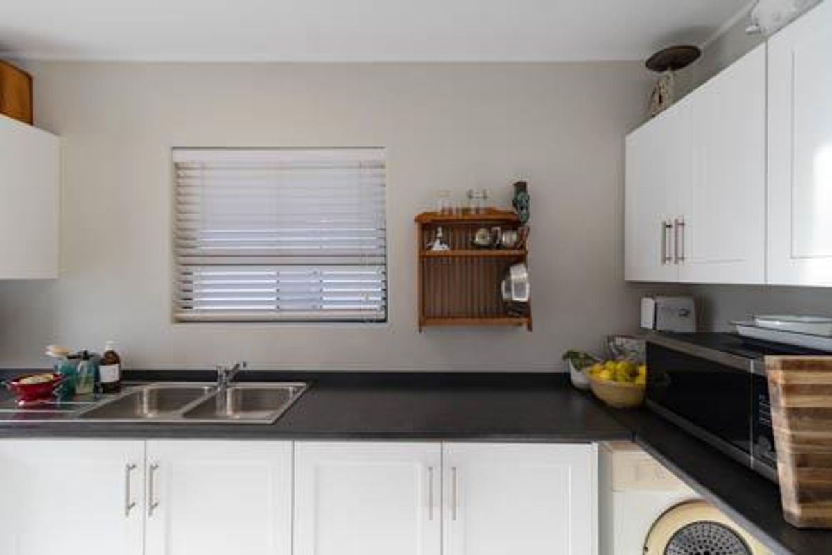 A functional kitchen area featuring white shaker-style cabinetry, dark laminate countertops, a double stainless steel sink, and a built-in microwave.