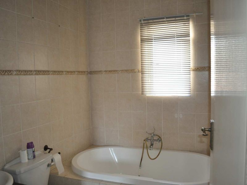 A functional bathroom featuring a built-in bathtub, wall-mounted shower mixer, and neutral ceramic wall tiling with a window blind.