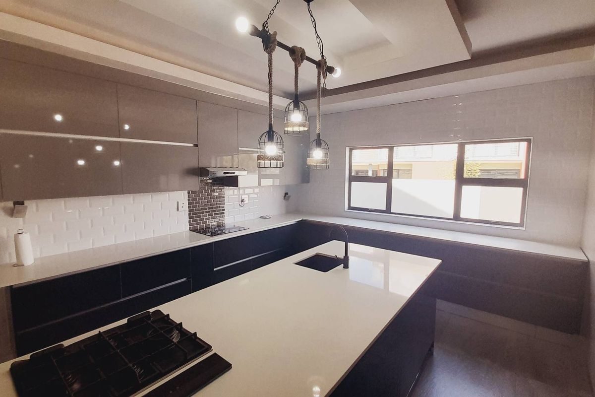 Modern kitchen featuring a central island with a built-in gas hob, sleek cabinetry, stone countertops, and a stylish pendant lighting fixture.