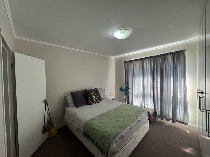 A functional bedroom featuring built-in cupboards, carpeted flooring, and natural light through window curtains.