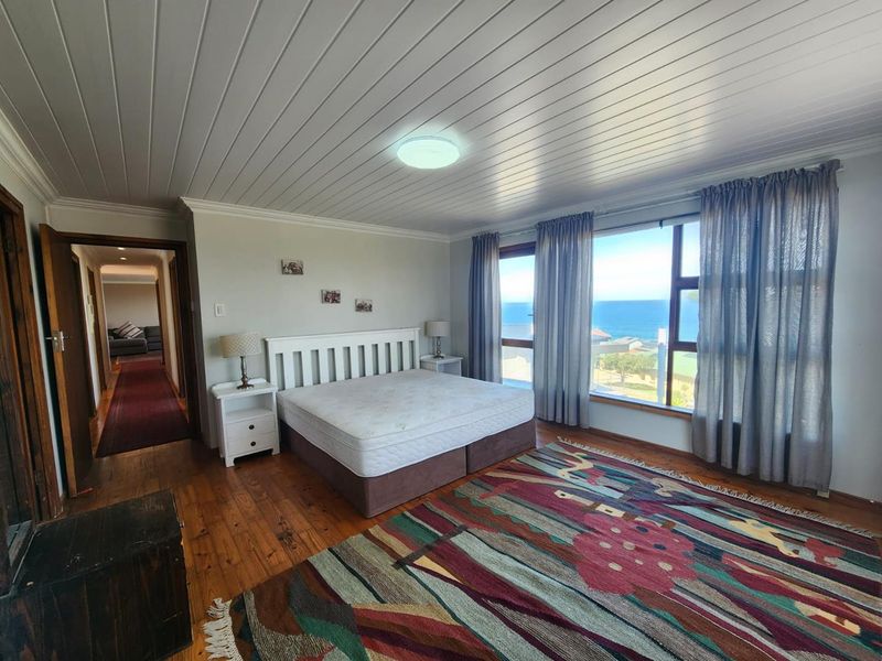Spacious bedroom featuring timber flooring, a tongue and groove ceiling, and large windows offering expansive ocean views.