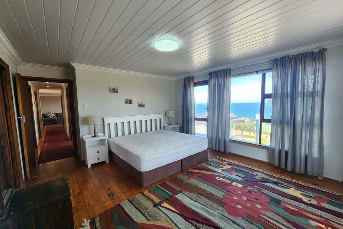 Spacious bedroom featuring timber flooring, a tongue and groove ceiling, and large windows offering expansive ocean views.