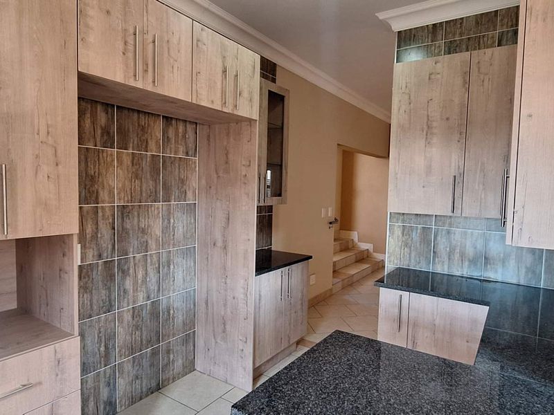 A modern kitchen featuring wood-look cabinetry, dark granite countertops, and tiled splashbacks, offering a clean and functional layout.
