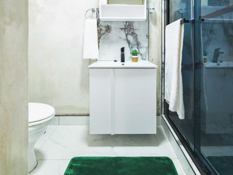 A compact bathroom featuring a modern white vanity with a black mixer tap, marble-look splashback, toilet, and a glass-enclosed shower.